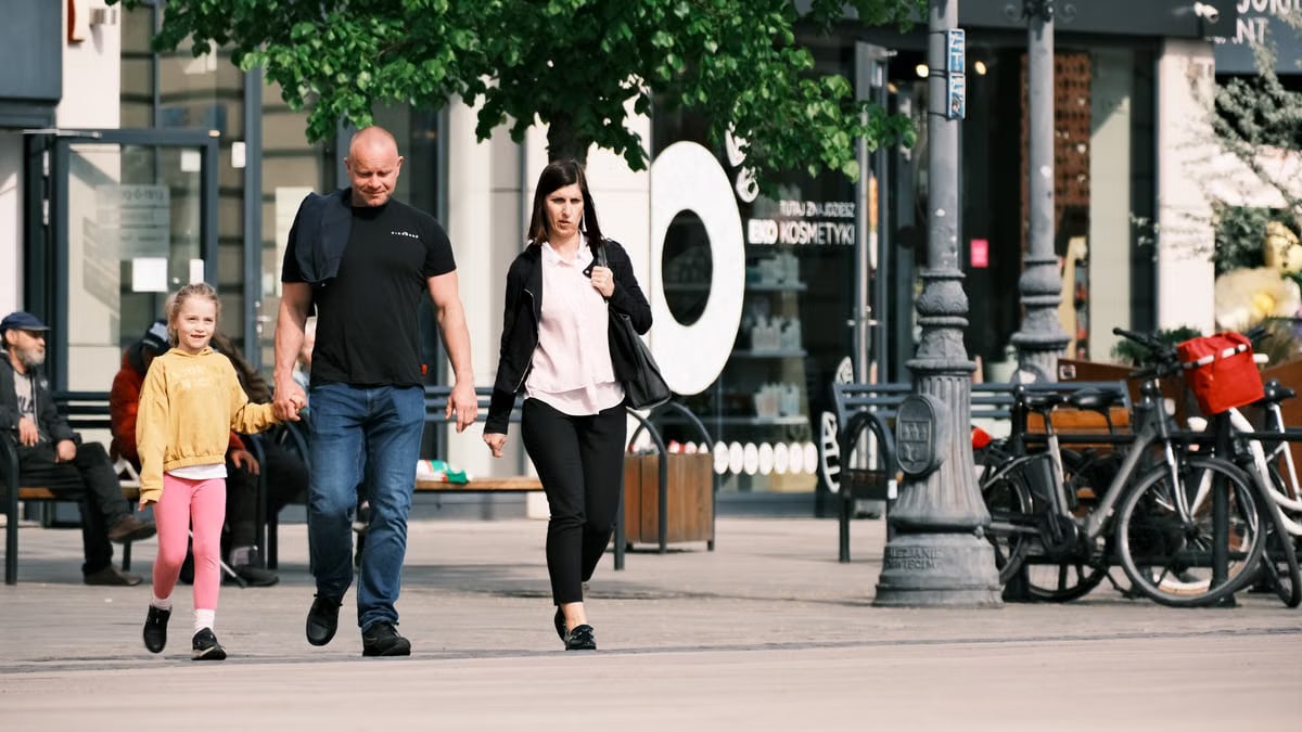 A family walks past storefronts and bicycles in a lively shopping district.
